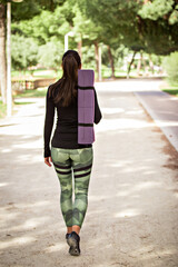 Young female walking in the park with a yoga mat over her shoulder.