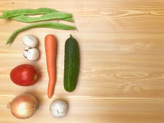Composición receta verduras frescas con bol, tenedor y cuchillo, utensilios de cocina en fondo de madera clara. Vegetariano. Pimiento, pepino, berenjena, zanahorias, ajo, judias verdes, tomate