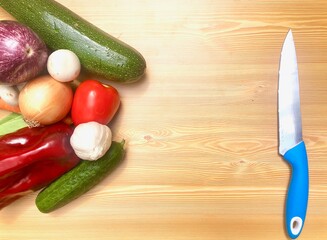 Verduras frescas de la huerta: pimiento, pepino, berenjena, zanahorias, ajo, judias verdes, tomate. Sobre fondo madera clara mesa. Con cuchillo y tenedor.