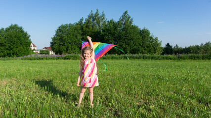 A  cheerful girl with a kite stands in the meadow during the summer holidays. Ideas for a leisure time with kids in a summer camp. Summer fun ideas for children. Kite launching.