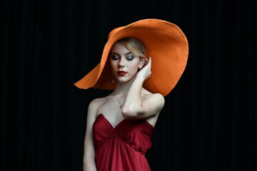 beautiful girl in a wide-brimmed hat and in a burgundy evening dress posing on a black background