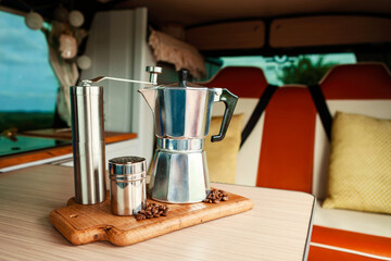Aqua Bialetti stovetop coffee maker, coffee grinder, chocolate shaker and coffee beans on a wooden tray in a cosy camper van