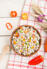 Pearl barley porridge with vegetables in wooden bowl on a white wooden background and linen textile. Top view, close up.