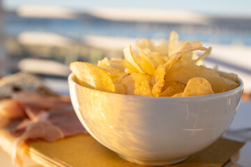 Afternoon aperitif on the beach in Italy. A wooden tray with a cup of potato crisps, and some...