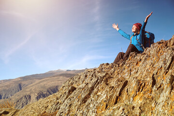Obraz premium Hiker woman with backpack sitting on rock of a mountain and enjoying sunrise