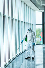 Coronavirus Pandemic. A disinfector in a protective suit and mask sprays disinfectants in office....