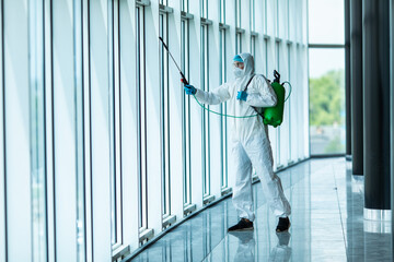 Coronavirus Pandemic. A disinfector in a protective suit and mask sprays disinfectants in office....