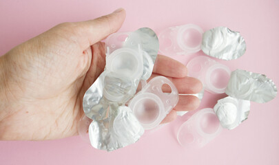 plastic, used containers, from under contact lenses, lie on the palm of a young girl, on a pink background. Vision problems, an alternative to glasses, eye comfort, increased cost of contact lenses