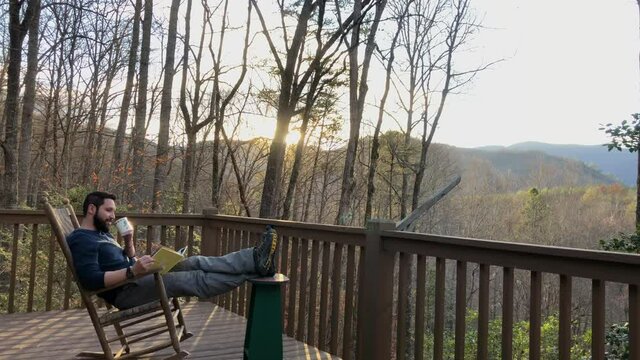 506 Man relaxing in a cabin in the woods while reading a book and drinking coffee