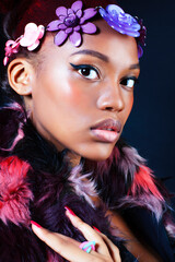 young pretty african american woman in spotted fur coat and flowers jewelry posing on black...