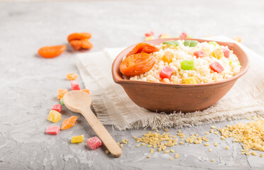Bulgur porridge with dried apricots and candied fruits in clay bowl on a gray concrete background and linen textile. Side view, selective focus.
