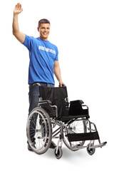 Cheerful man volunteer waving and standing with an empty wheelchair