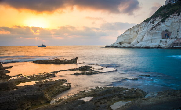Beautiful sunset with white cliffs of Rosh HaNikra grottoes, on the border between Israel and Lebanon, on the coast of the Mediterranean Sea, with Israeli Navy border patrol boat; Western Galillee