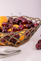 The fruits of the cherries and apricots in a wicker basket on a white background.