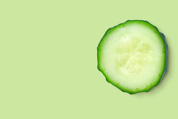 One slice closeup of fresh organic cucumber isolated on a green background. The concept of freshness, juiciness,diet. Top view with copy space.