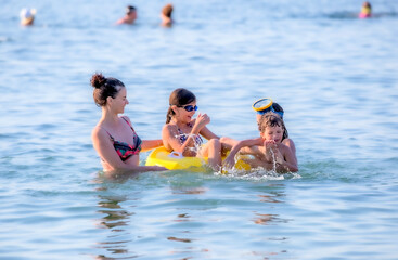 Mother and sun in the sea. Summer holidays on the sea beach. Happy family swims in the sea. Mom with children in the water.