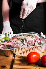 Raw meat in an aluminum dish on a wooden table against a background of rustic utensils
