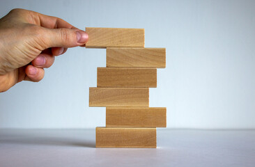 Concept of building success foundation. Men hand put wooden blocks on the stack of wooden blocks. Beautiful white background, copy space.