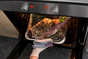 Meat steak baked in foil with fresh herbs and vegetables.  Woman's hand gets out of the oven....