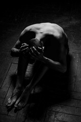 The man sits bent over in the shape of a skull. Silhouette of a seated man. The figure of a sitting guy in the shape of a skull. A guy holding his head.