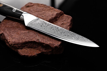 A large kitchen knife with a black handle on a dark background. Knife with a wide sharp blade. Scratched steel surface of the knife blade. - obrazy, fototapety, plakaty