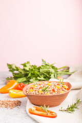 Buckwheat porridge with vegetables in clay bowl on a gray and pink background and linen textile. Side view, copy space, selective focus.