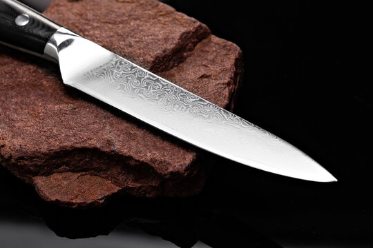 A large kitchen knife with a black handle on a dark background. Knife with a wide sharp blade. Scratched steel surface of the knife blade.