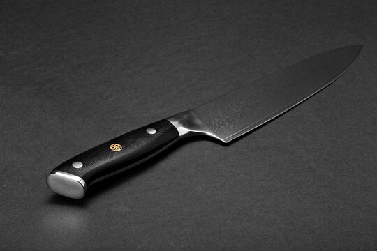 A large kitchen knife with a black handle on a dark background. Knife with a wide sharp blade. Scratched steel surface of the knife blade.