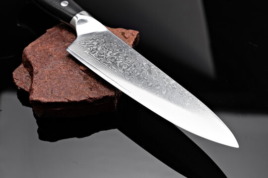 A large kitchen knife with a black handle on a dark background. Knife with a wide sharp blade. Scratched steel surface of the knife blade. 
