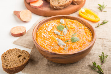 Sweet potato or batata cream soup with sesame seeds in a wooden bowl on a white wooden background. side view, selective focus.