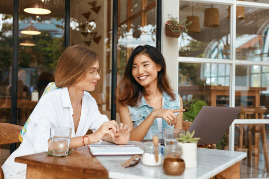 Girls At Coffee Shop. Women Having Call On Laptop At Cafe. Beautiful Colleagues In Casual Clothes Chatting At Comfortable Workplace On Summer Vacation. Modern Technologies For Digital Nomad Lifestyle.
