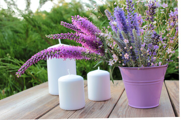 Bunch of purple summer flowers and candles. Lavender, veronica in a decorative bucket on wooden table in the garden.
