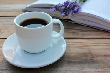Cup of coffee, open book and bunch of purple lavender flowers on wooden table in the garden. Selective focus. Copy space
