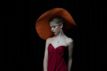 beautiful girl in a wide-brimmed hat and in a burgundy evening dress posing on a black background