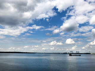 Blue sky, white clouds above the water and a small barge.
