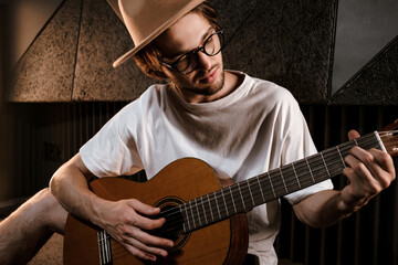 Portrait of attractive male musician intently playing on guitar in recording studio. Handsome stylish guy composing song in modern sound studio