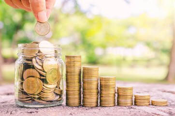 investor business man hand putting coins in jar on wood table with blur nature park background....
