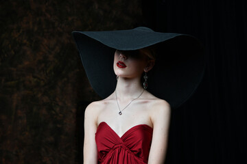 beautiful girl in a wide-brimmed hat and in a burgundy evening dress posing on a black background