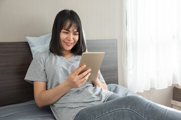 Asian woman touch tablet on bed and smile