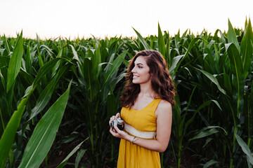 portrait of young beautiful woman wearing a yellow dress standing in a green corn field. Summertime and lifestyle