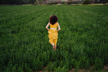 portrait of young beautiful woman wearing a yellow dress running in a green field. Summertime and lifestyle