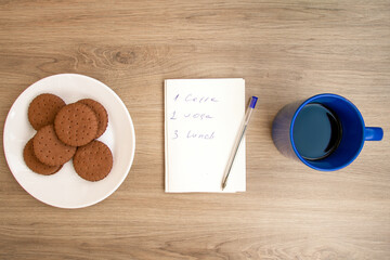 Good morning with coffee. A cup of coffee in blue. Biscuits.  Notepad with daily routine. . Sunny.