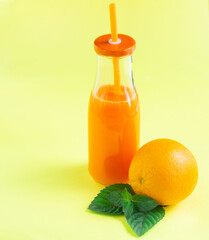 Minimalistic composition. Bright, juicy image. Fresh citrus juice with mint in a glass bottle with a tube. Yellow background. Empty space for text