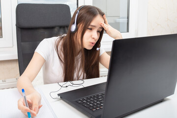 The difficulties of online education. A student at home is engaged in training with headphones, does not understand anything