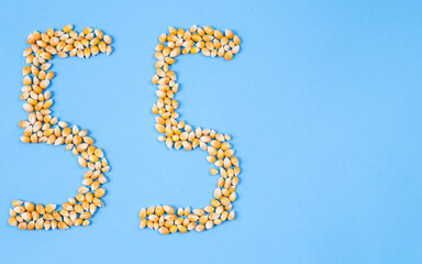 number 55 made from corn on the left and with place for text on the right on a blue background, close-up top view.