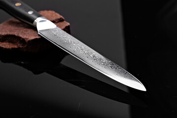 A large kitchen knife with a black handle on a dark background. Knife with a wide sharp blade....
