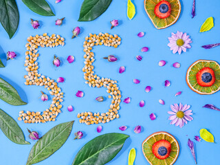 Numeral 55 with berries, fruits and flowers on a blue background, close-up top view.