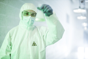 Corona virus concept. Male scientist doctor in mask, glasses and protective suit reviewing COVID-19 test-tube with blue liquid during pandemic outbreak. Man in biochemistry laboratory