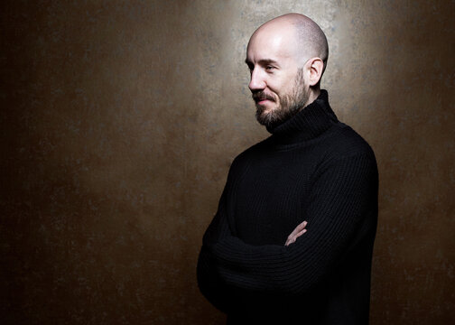 Fashion Portrait of a 40-year-old man standing over a light gray background in a black sweater. Close up. Classic style. Bald shaved head. Copy-space. Studio shot