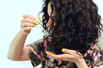 Woman applying natural oil on the tips of her curly hair, close up. Oil hair treatment for woman.